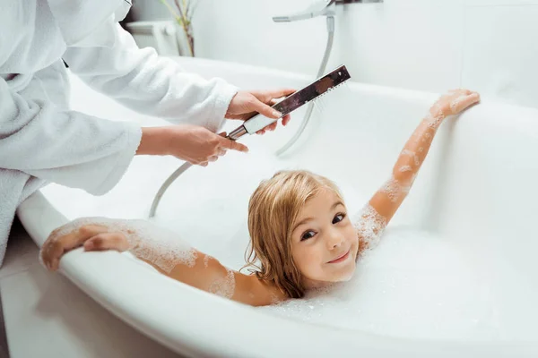 Niño adorable y desnudo tomando baño cerca de la madre en el baño - foto de stock