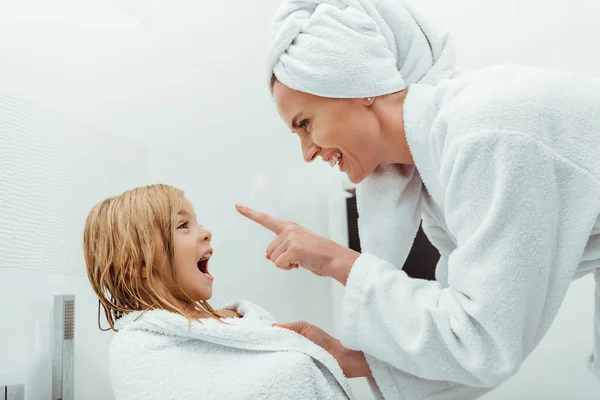 Mãe feliz apontando com o dedo perto da filha animada no banheiro — Fotografia de Stock