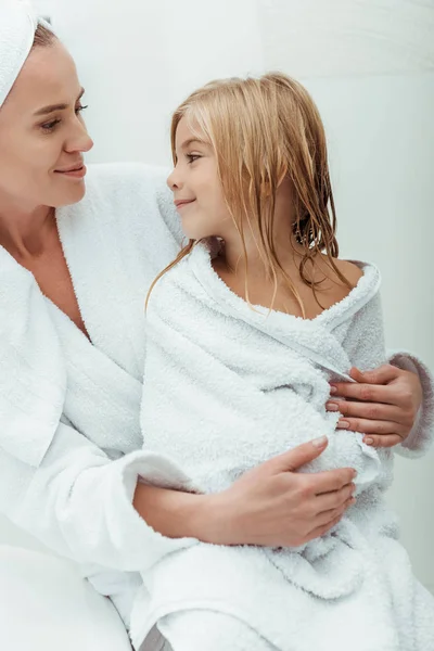 Feliz madre mirando lindo y mojado hija en cuarto de baño - foto de stock
