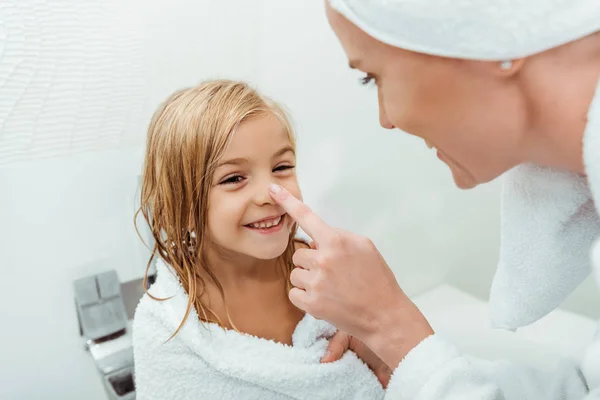 Selektiver Fokus der Mutter, die Nase ihrer glücklichen Tochter im Badezimmer berührt — Stockfoto