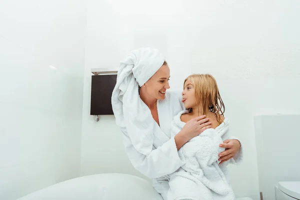 Happy mother smiling while looking cute daughter sticking out tongue — Stock Photo