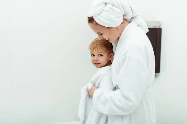 Happy mother smiling while hugging toddler son in bathroom — Stock Photo