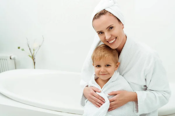 Glückliche Mutter lächelt, während sie den kleinen Jungen im Badezimmer umarmt — Stockfoto