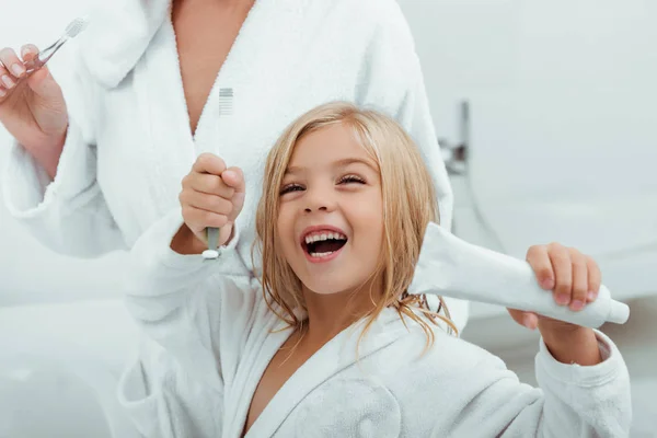 Selective focus of happy kid holding toothpaste near mother — Stock Photo