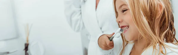 Panoramic shot of happy kid brushing teeth near mother — Stock Photo