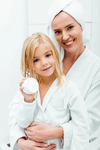 Feliz madre abrazando lindo niño sosteniendo contenedor con crema cosmética - foto de stock