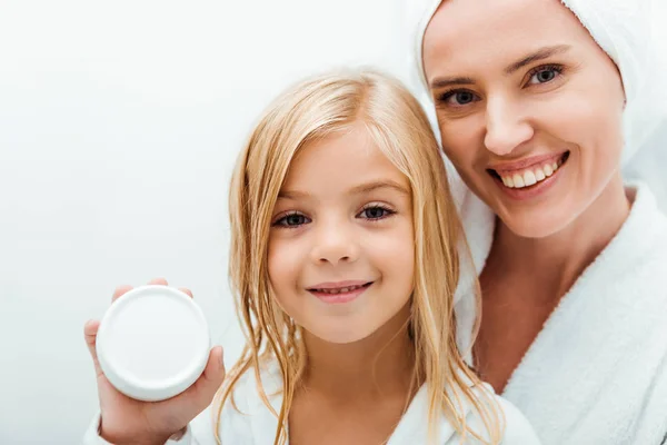 Mignon enfant tenant récipient avec crème cosmétique près de mère gaie en peignoir — Photo de stock