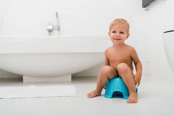 Menino criança feliz sentado no penico azul perto da banheira — Fotografia de Stock