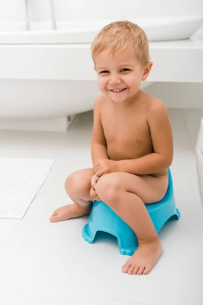 Усміхнений маленький хлопчик сидить на синьому горщику біля ванни — стокове фото