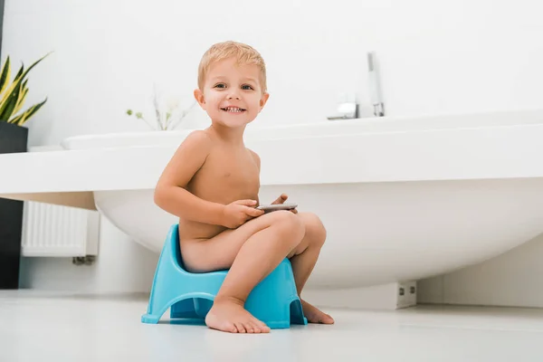 Happy toddler boy sitting on potty and using smartphone — Stock Photo