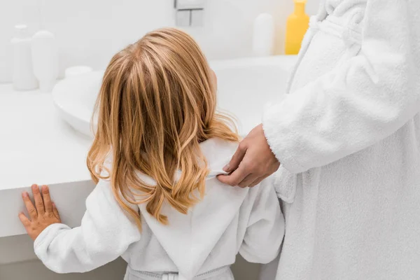 Visão traseira da filha em roupão de banho de pé com a mãe no banheiro — Fotografia de Stock