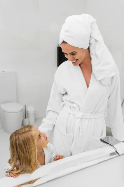 Glückliche Mutter im Handtuch schaut süße Tochter im Badezimmer an — Stockfoto