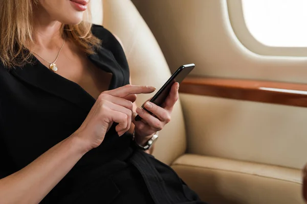 Cropped view of businesswoman using smartphone in private jet — Stock Photo