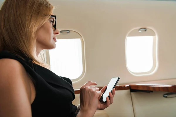 Side view of businesswoman holding smartphone in private plane — Stock Photo