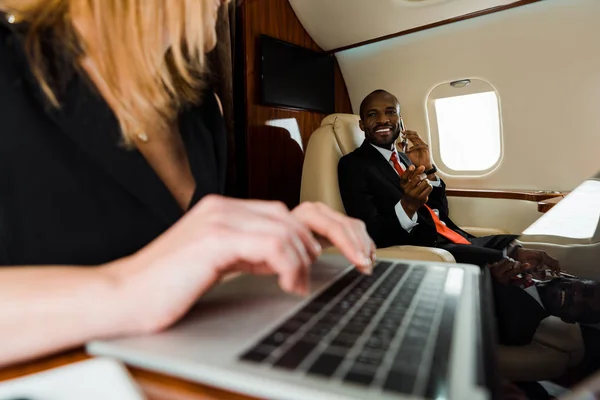 Selektiver Fokus eines afrikanisch-amerikanischen Geschäftsmannes, der mit Laptop im Privatflugzeug in der Nähe einer Geschäftsfrau gestikuliert — Stockfoto