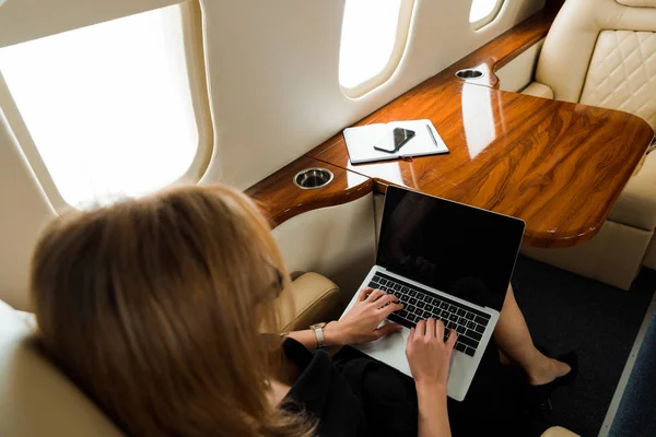 Vista aérea de la mujer de negocios utilizando el ordenador portátil con pantalla en blanco en jet privado - foto de stock