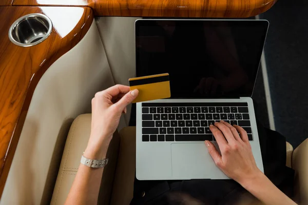 Vista recortada de la mujer de negocios con tarjeta de crédito cerca de la computadora portátil en jet privado - foto de stock