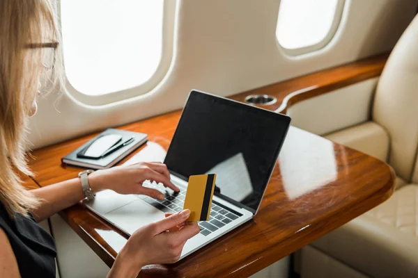 Обрезанный вид бизнесвумен с кредитной картой возле ноутбука в частном самолете — стоковое фото