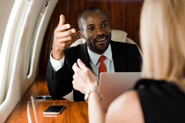 Selective focus of african american businessman gesturing near businesswoman in private plane — Stock Photo