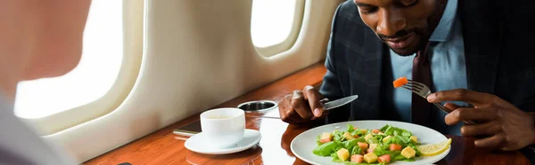 Panoramic shot of african american businessman near tasty dish and businesswoman in private plane — Stock Photo