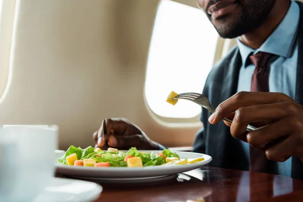 Vue recadrée de l'homme afro-américain mangeant de la salade en avion privé — Photo de stock