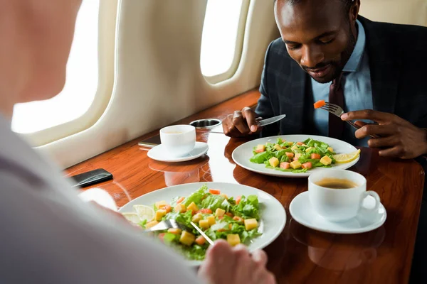 Вибірковий фокус афроамериканського бізнесмена біля смачних страв і бізнес-леді в приватному літаку — стокове фото