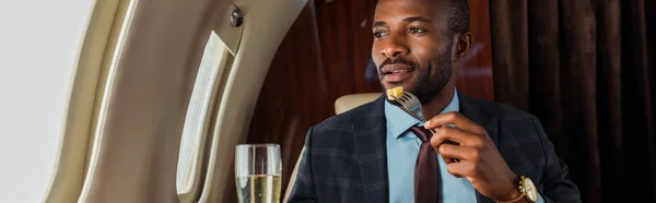 Plan panoramique de l'homme afro-américain mangeant en jet privé — Photo de stock