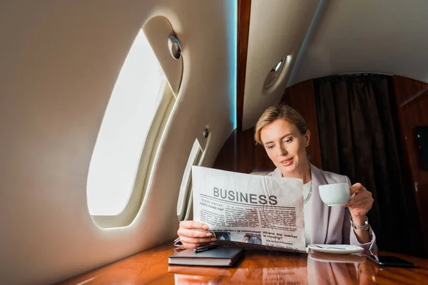 Beautiful businesswoman holding cup while reading business newspaper in private plane — Stock Photo