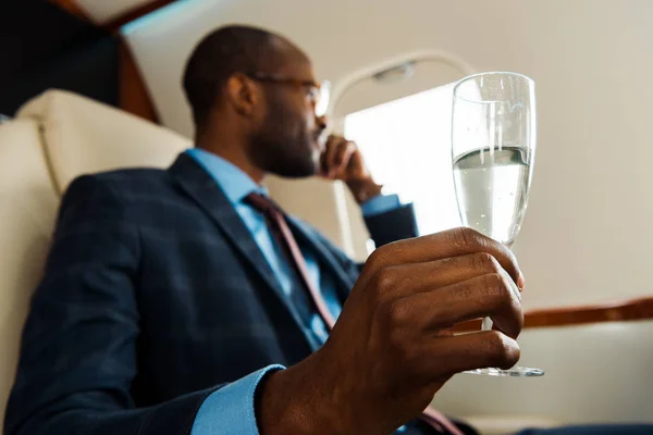 Messa a fuoco selettiva dell'uomo afro-americano in possesso di bicchiere di champagne in aereo privato — Foto stock