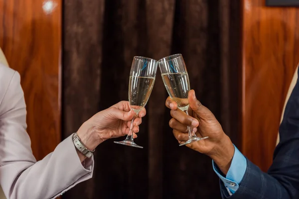 Vue recadrée de l'homme et de la femme afro-américains cliquetis verres à champagne dans un avion privé — Photo de stock