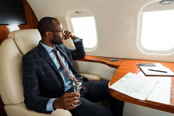 Schöner afrikanisch-amerikanischer Mann in Gläsern mit Champagnerglas im Privatflugzeug — Stockfoto