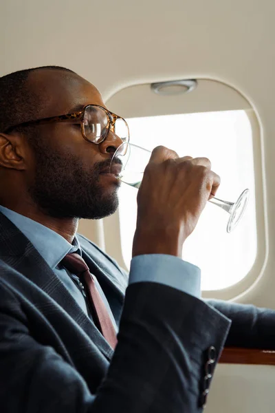 Handsome african american businessman in glasses drinking champagne in private jet — Stock Photo