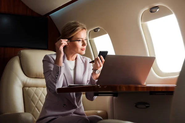 Donna d'affari che applica mascara vicino al computer portatile in aereo privato — Foto stock
