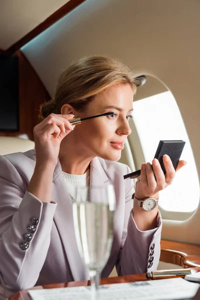 Selective focus of businesswoman applying mascara in private plane — Stock Photo