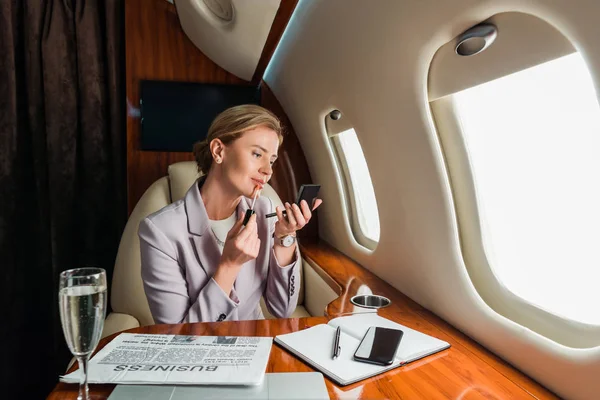 Atractiva mujer de negocios aplicando brillo labial en avión privado - foto de stock