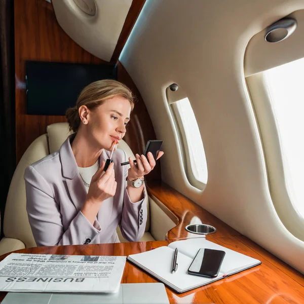 Atractiva mujer de negocios aplicando brillo labial en jet privado - foto de stock