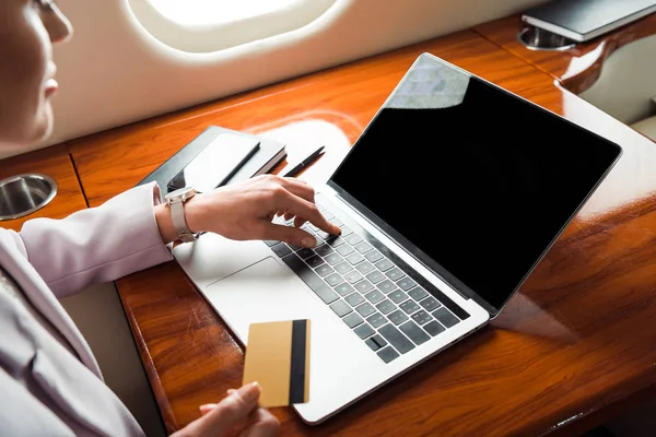 Vista recortada de la mujer de negocios utilizando el ordenador portátil con pantalla en blanco y la celebración de la tarjeta de crédito en avión privado - foto de stock