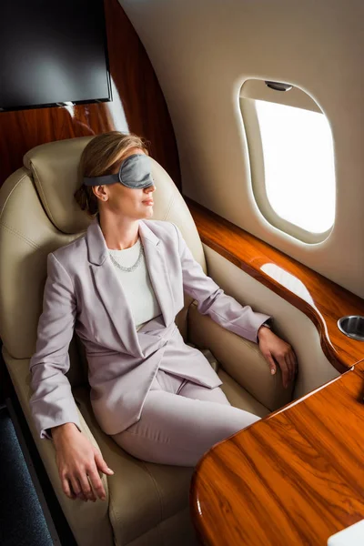 Femme d'affaires avec masque de couchage assis près de la fenêtre de l'avion en avion privé — Photo de stock