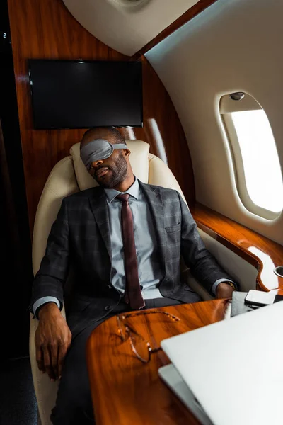 Empresário afro-americano com máscara de dormir sentado em avião privado — Fotografia de Stock