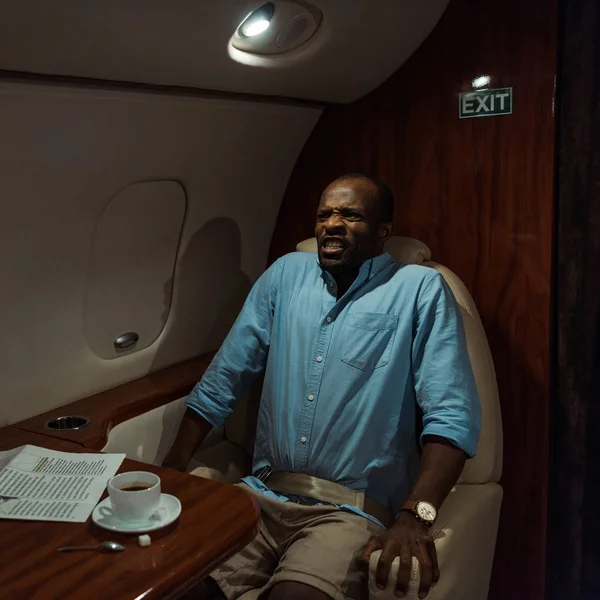 Напружений афроамериканський чоловік з страхом від польоту сидить у приватному літаку — стокове фото