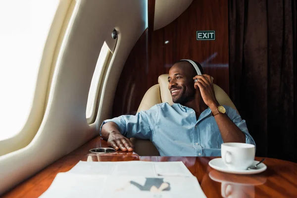 Selective focus of happy african american man listening music in private plane — Stock Photo