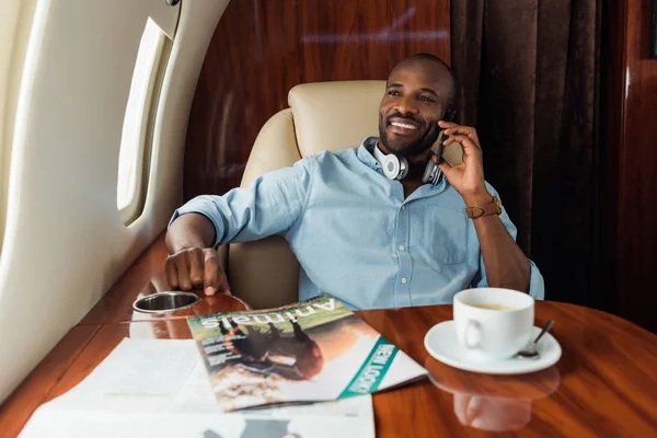 Счастливый африканский американец разговаривает на смартфоне возле чашки с напитком — стоковое фото