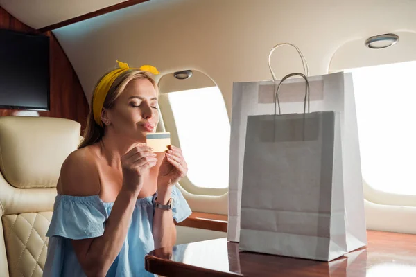 Happy girl holding credit card near shopping bags in private plane — Stock Photo