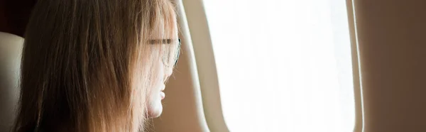 Панорамний знімок бізнес-леді в окулярах дивиться на вікно літака — стокове фото