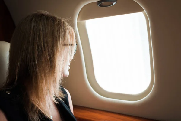Businesswoman in glasses looking at airplane window — Stock Photo