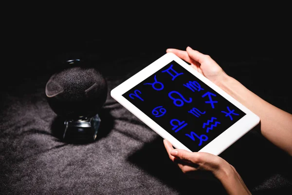 Cropped view of astrologer holding digital tablet with zodiac signs near crystal ball on black velvet cloth — Stock Photo