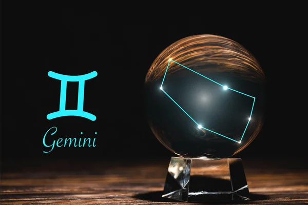 Crystal ball with constellation near Gemini zodiac sign on wooden table isolated on black — Stock Photo