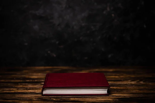 Red book on wooden table on black background — Stock Photo