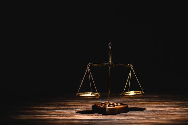 Golden scales of justice on wooden table on black background — Stock Photo