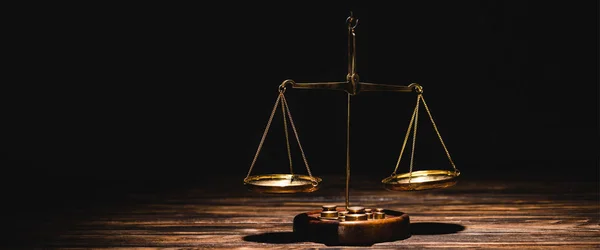 Golden scales of justice on wooden table on black background — Stock Photo